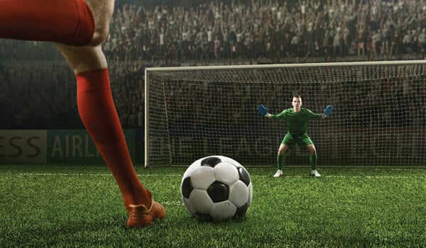 Soccer player about to kick a ball toward a waiting goalie in a goal