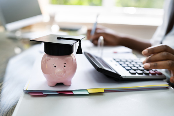 Piggy bank wearing graduation cap, person using calculator