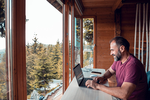 Man using a laptop in a cabin overlooking a forest