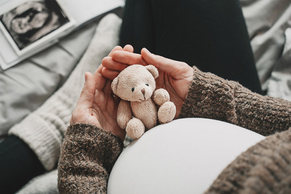Woman pregnant belly with little teddy toy bear